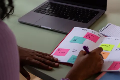 Person arranges sticky notes in a calendar next to a laptop