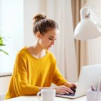 A person in a yellow sweater types on a laptop