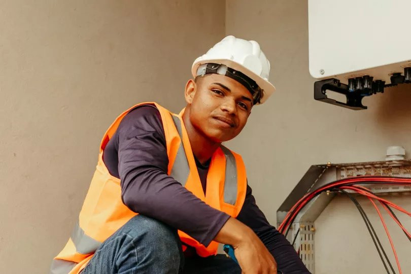 A person in a hardhat and high-visibility vest holds a wire