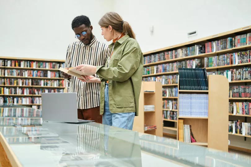 Two people converse over a book in a library