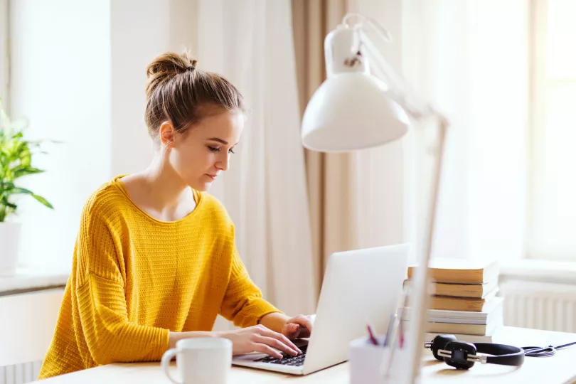 A person in a yellow sweater types on a laptop