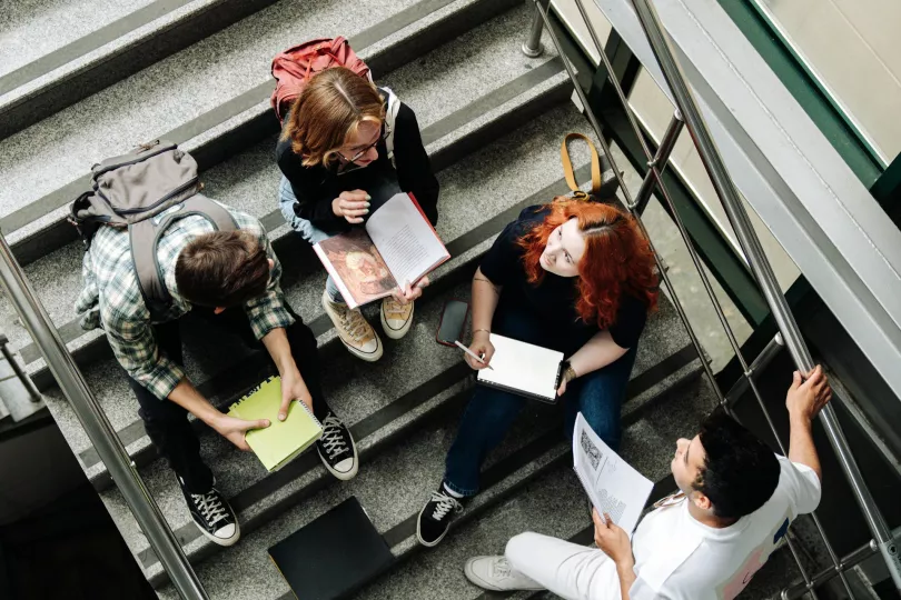Several people sit on a staircase in an academic setting