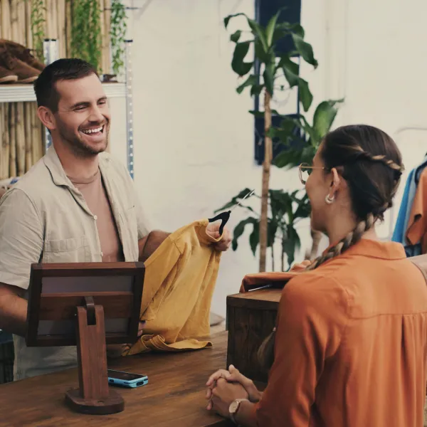 Fashion, cashier and man in shop with customer, small business sales with friendly smile at pos and shopping