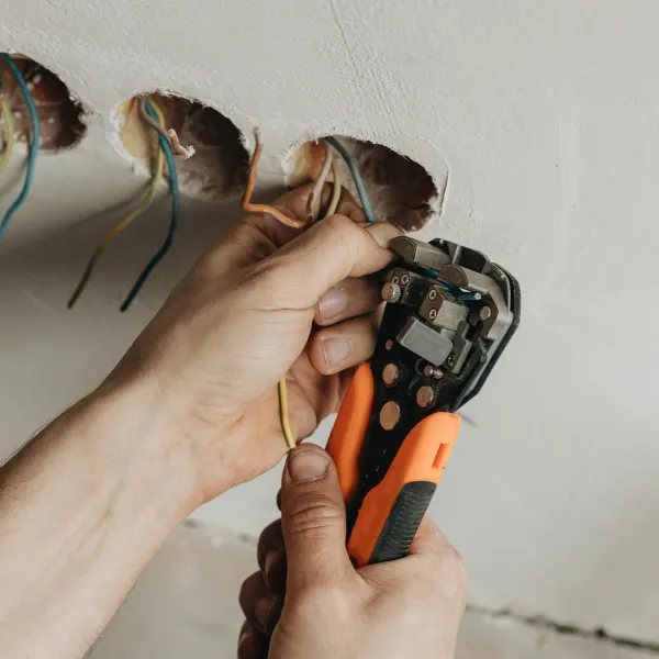 An electrician uses a tool to adjust wiring in a wall