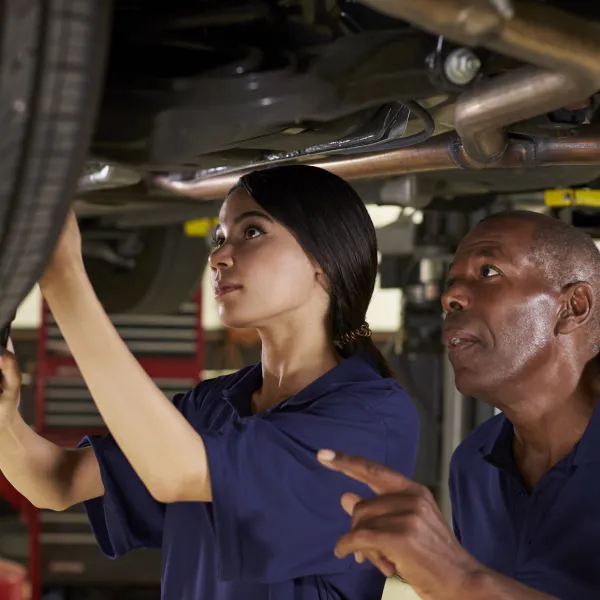 Mechanic And Female Trainee Working Underneath Car Together