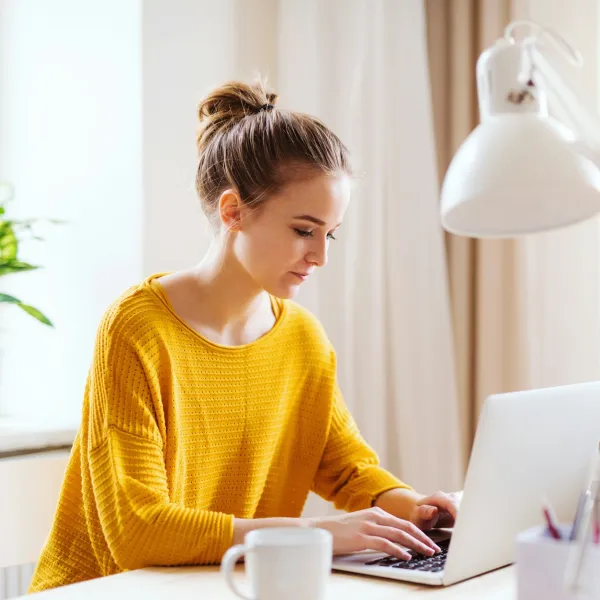 A person in a yellow sweater types on a laptop