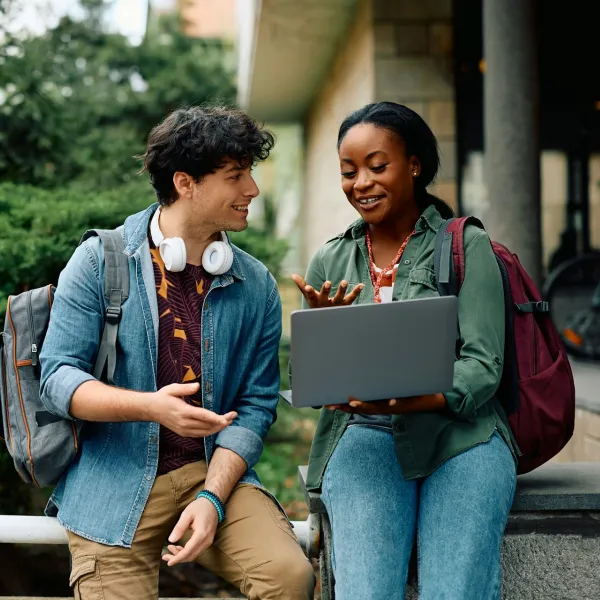 Two people converse in an academic setting; one holds a laptop