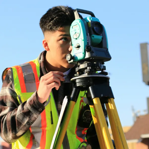 A person in a safety vest looks through a total station