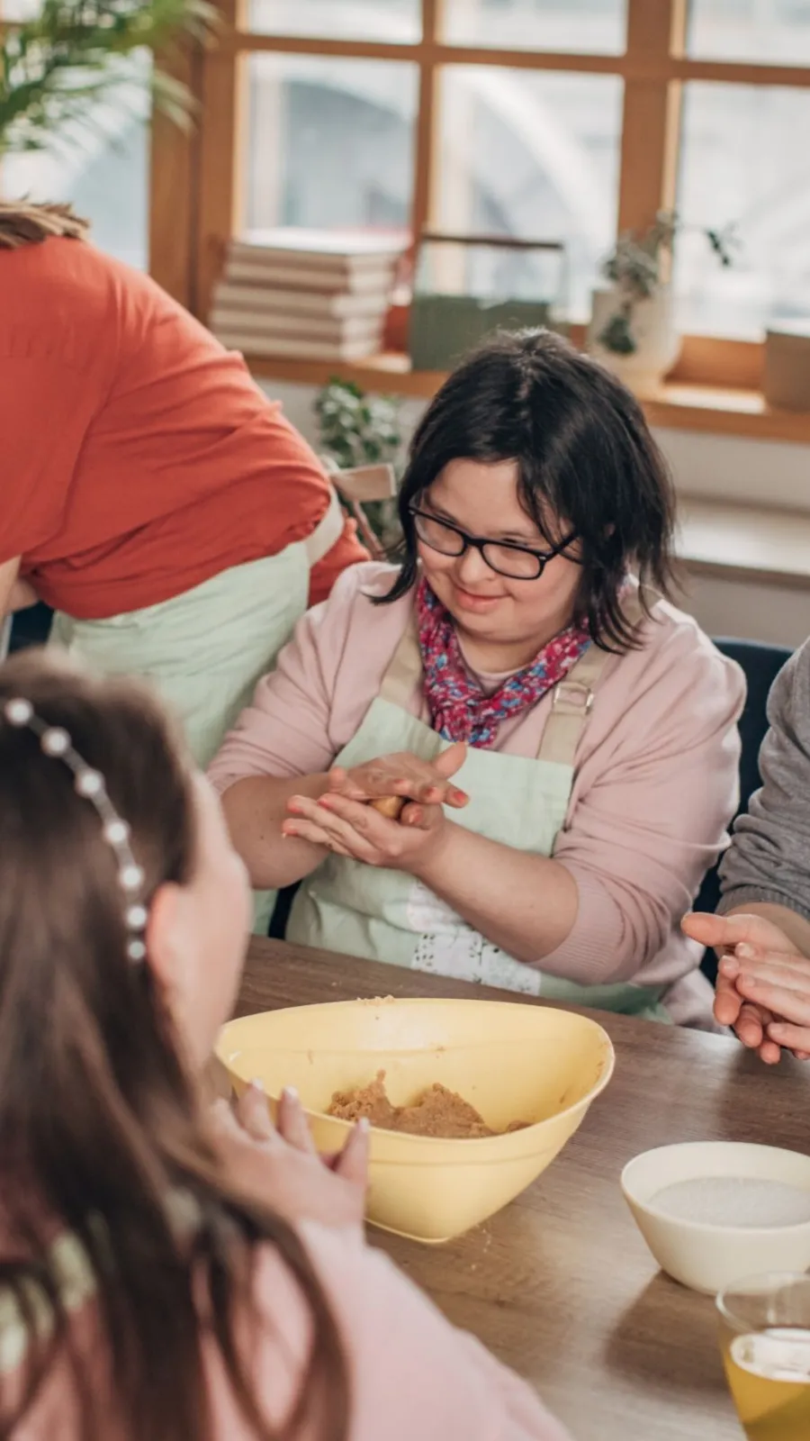 People wearing aprons sitting around a table shaping dough together during a cooking class.