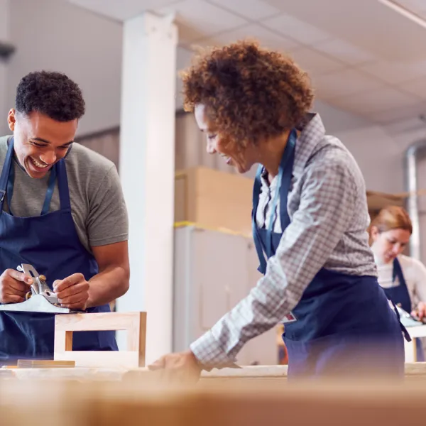 Female Instructor With Carpentry Student In Workshop Studying For Apprenticeship At Colleg