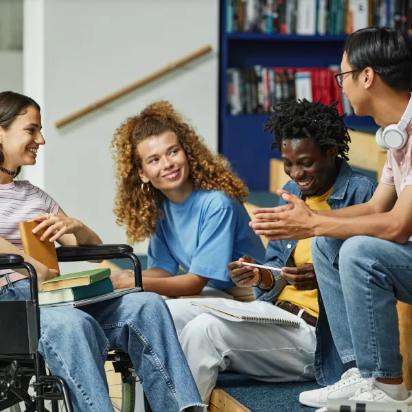 Diverse group of young people chatting in college library including female student with disability