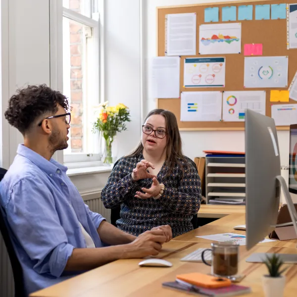 a young adult female with Down syndrome and her mid-adult male colleague sitting at a desk in an office